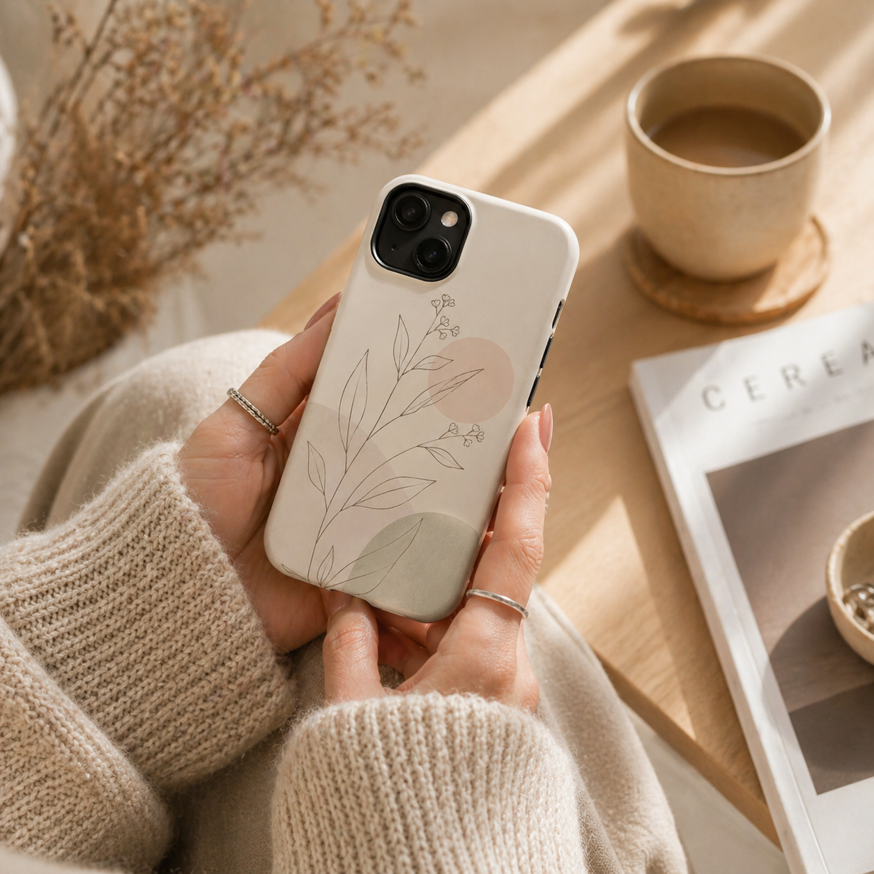 Person holding a phone with a floral case in a cozy setting with a cup of coffee and a magazine.