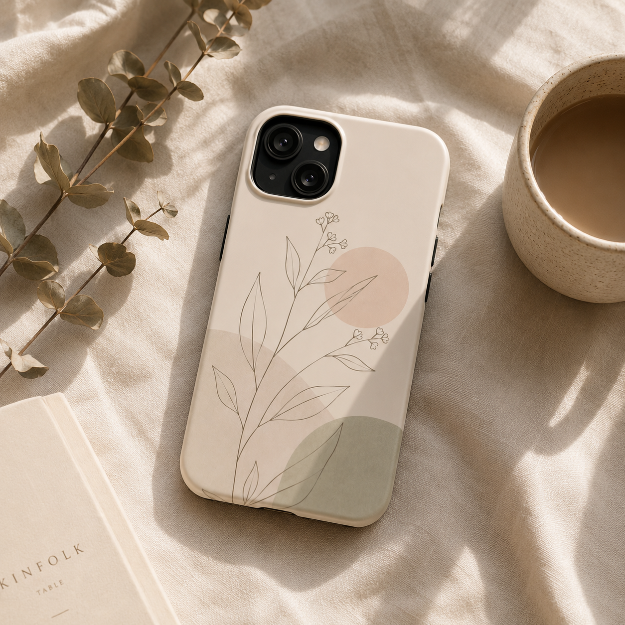 Phone case with floral design on a beige surface with a cup of coffee and book