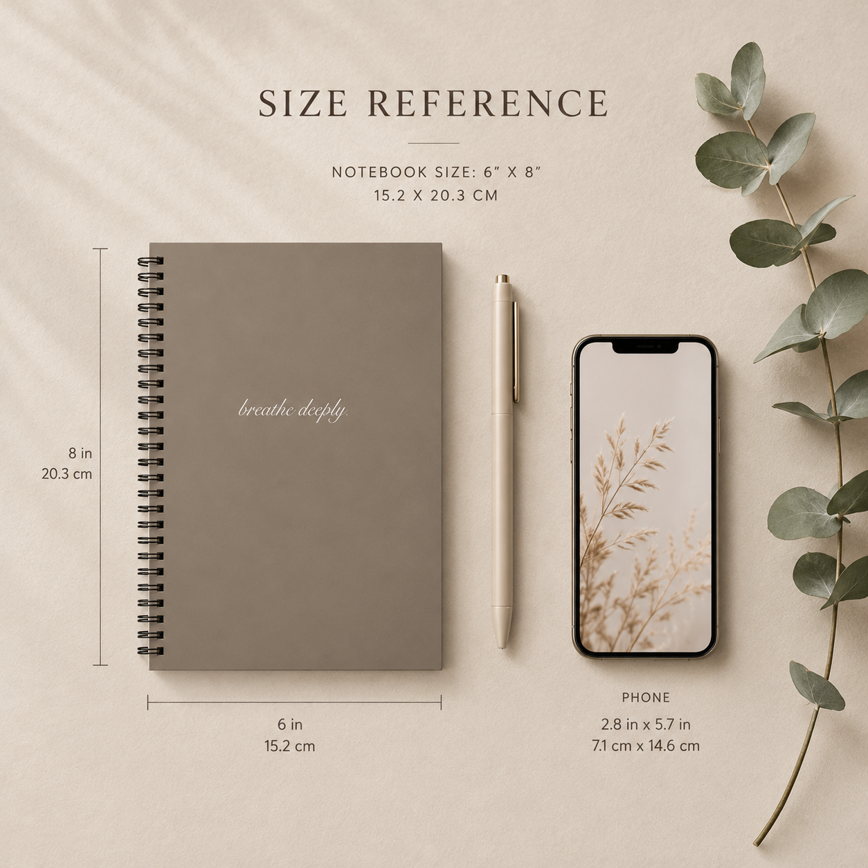 Notebook, phone, pen, and eucalyptus leaves on a beige background with size reference text.