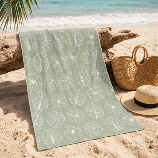 Green beach towel with leaf pattern on sand by the ocean