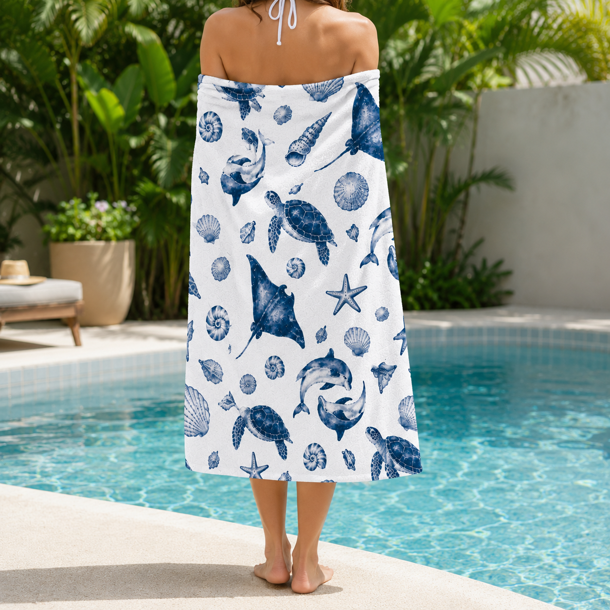Person wrapped in a white towel with blue ocean-themed pattern by a pool