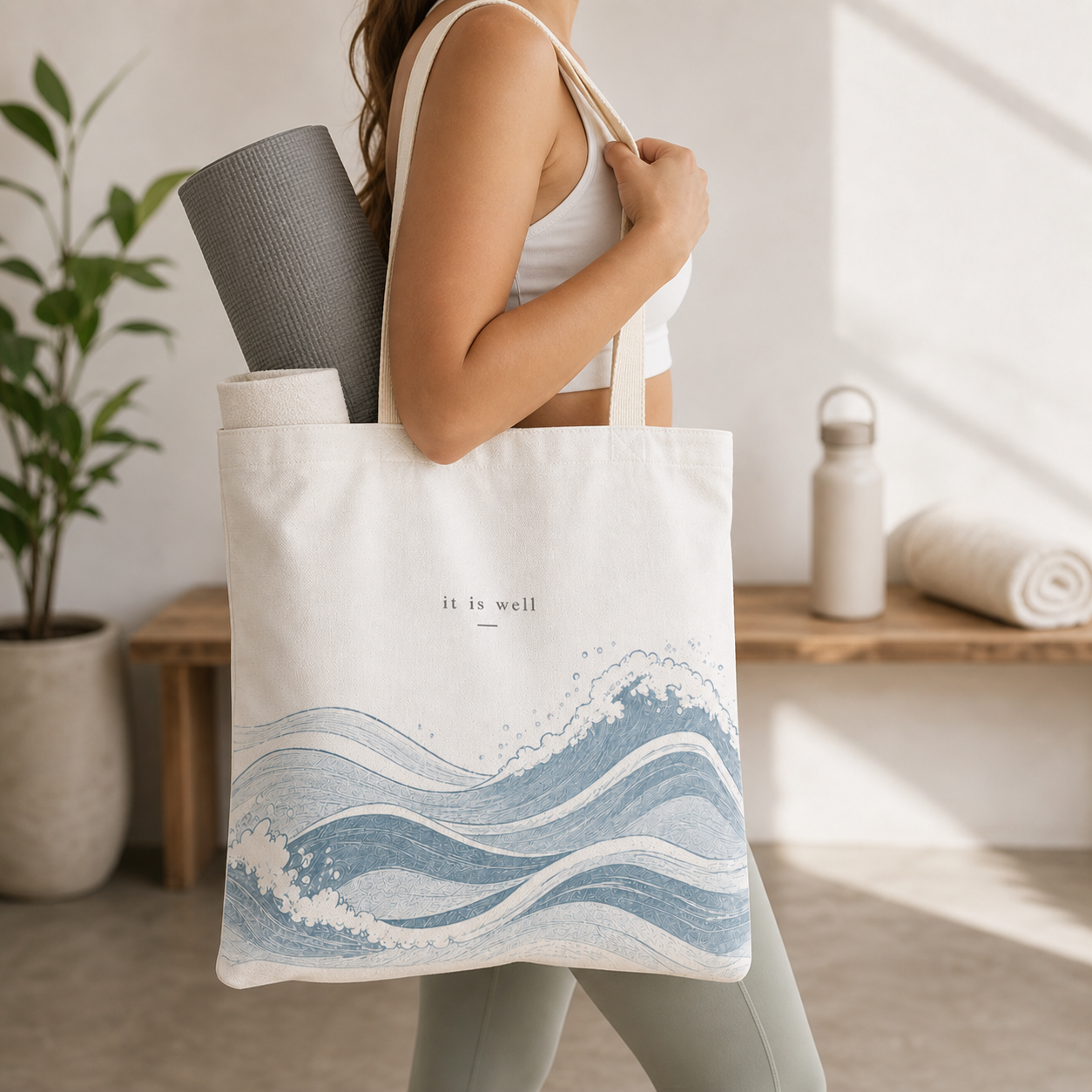 Person holding a tote bag with wave design and 'it is well' text, indoor setting.