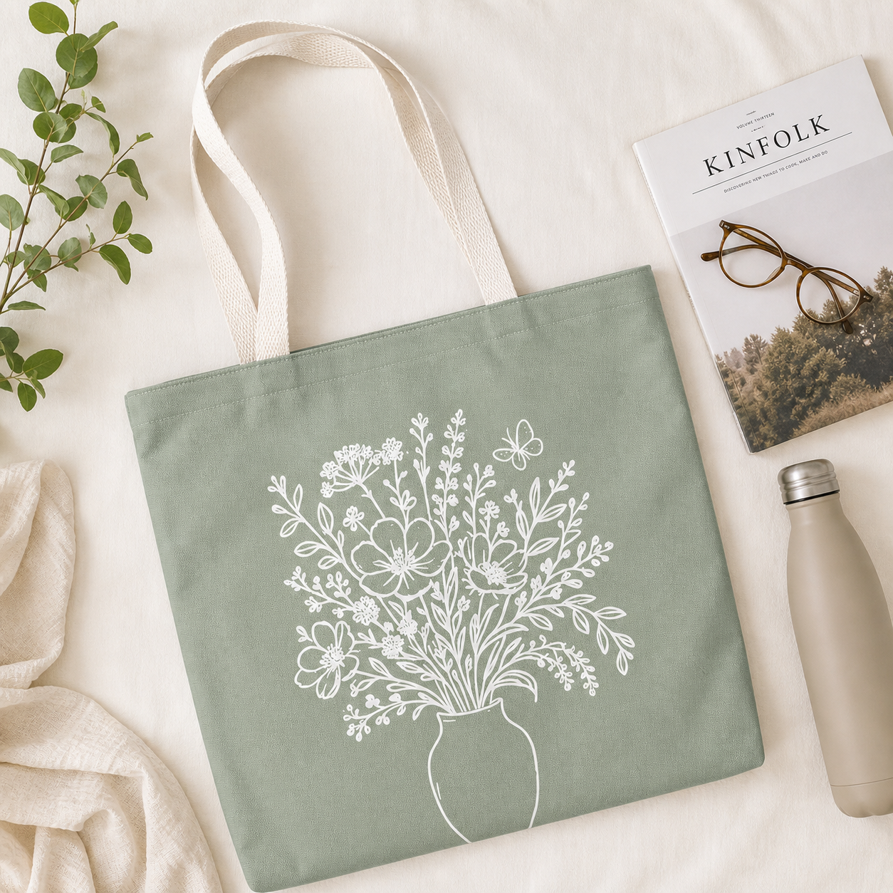 Green tote bag with floral design, Kinfolk magazine, glasses, and water bottle on a light background