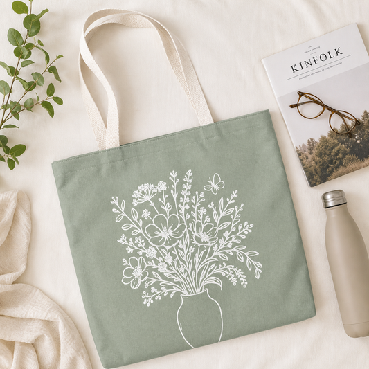 Green tote bag with floral design, Kinfolk magazine, glasses, and water bottle on a light background