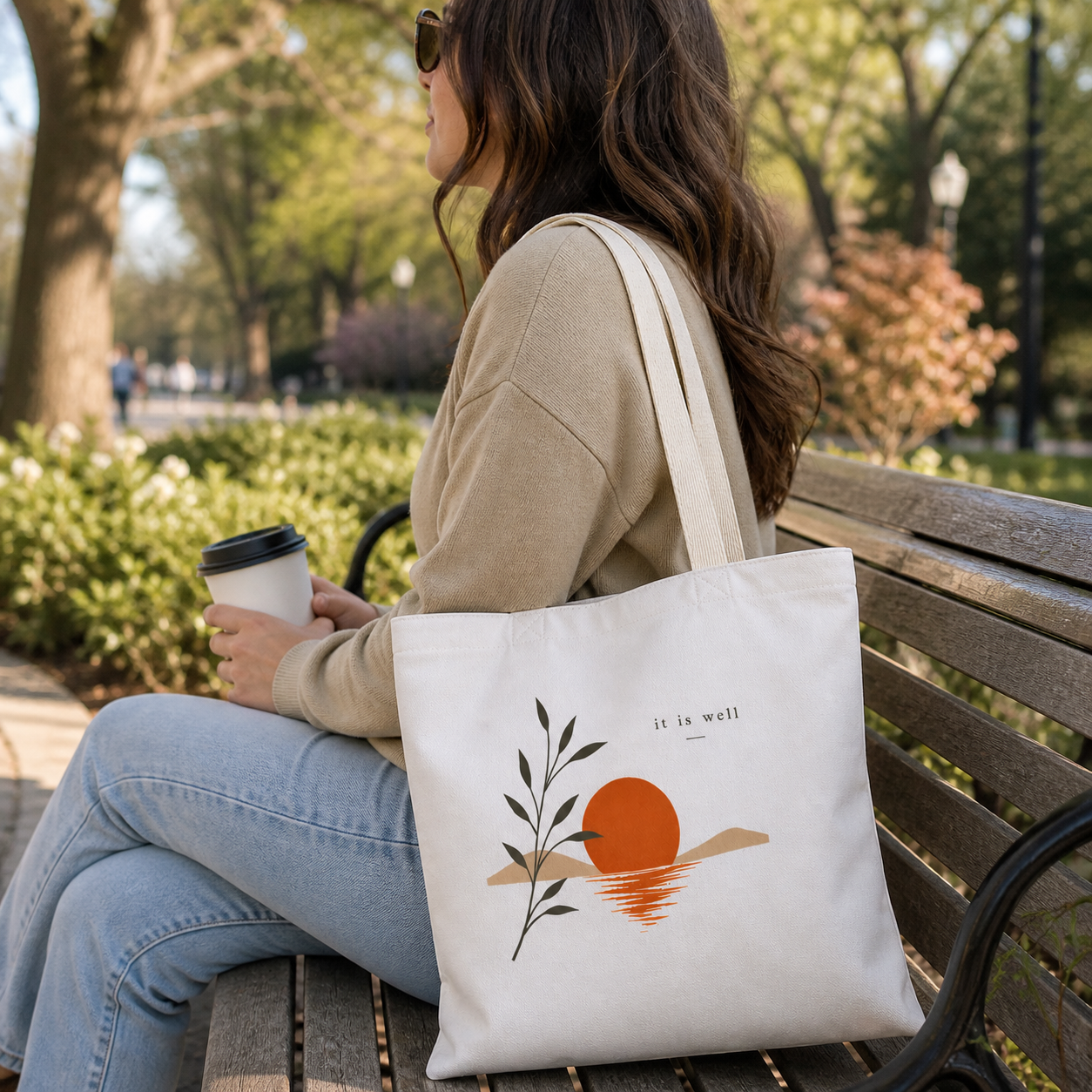 Woman sitting on a bench with a tote bag and coffee cup in a park