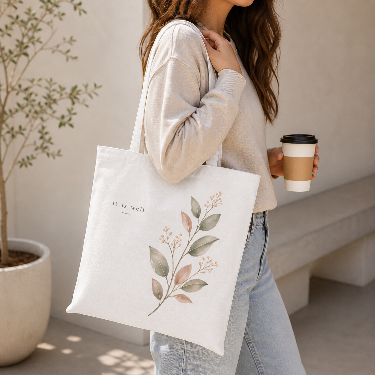 Person holding a tote bag with floral design and text, standing indoors.
