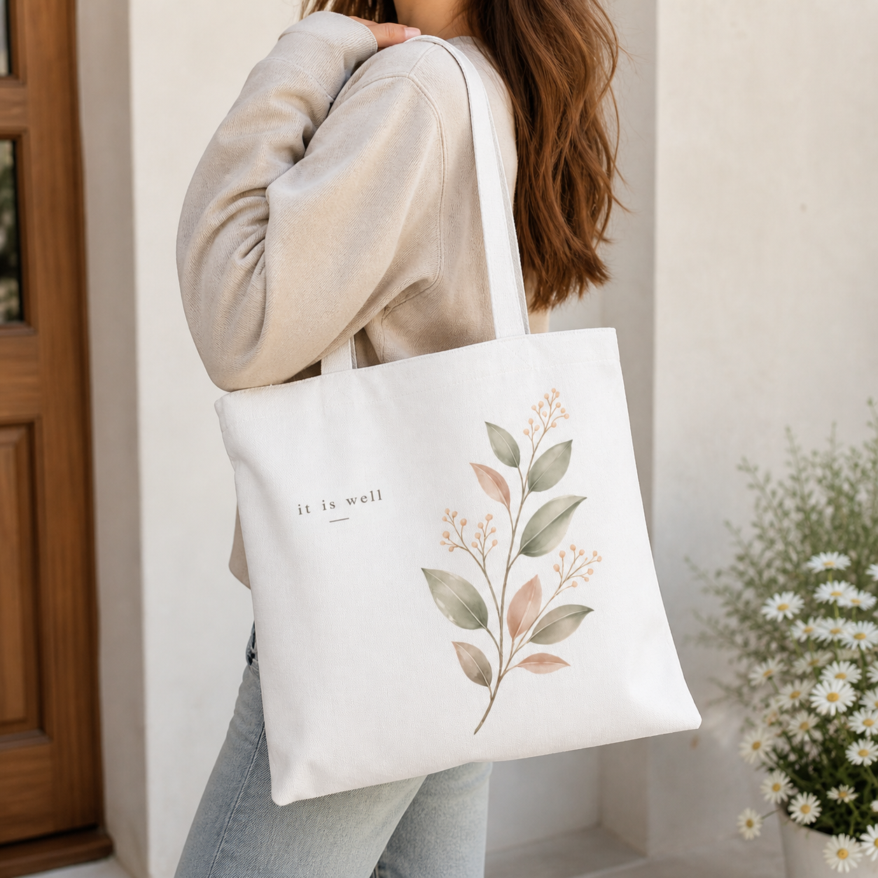 Person holding a white tote bag with floral design and 'it is well' text.