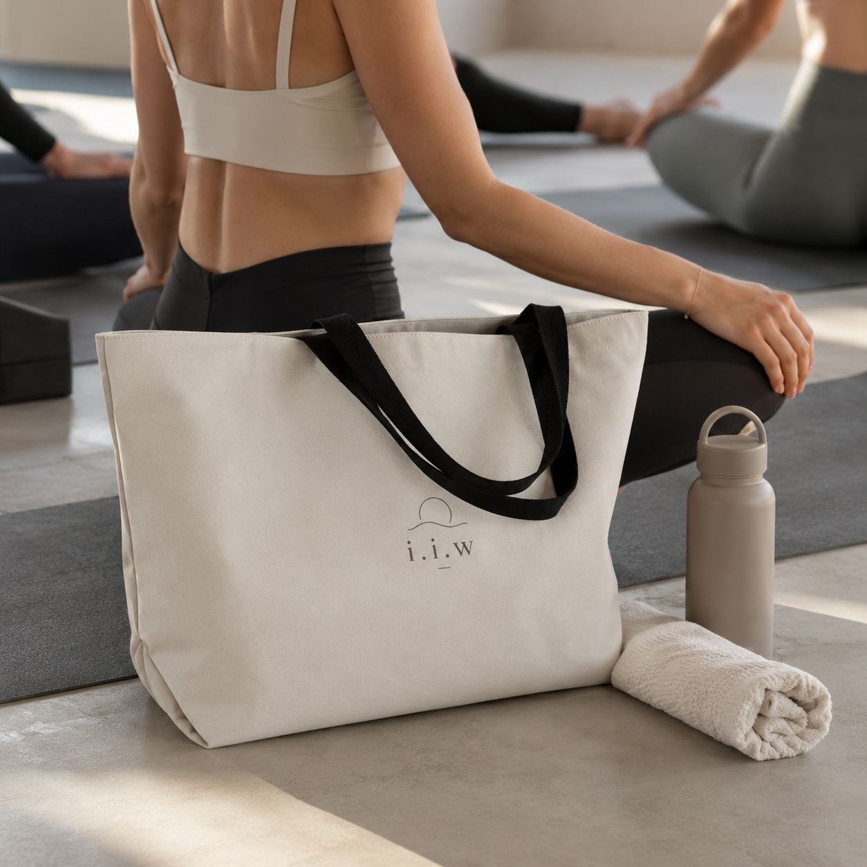 Person sitting on a yoga mat with a tote bag and water bottle in a yoga studio.