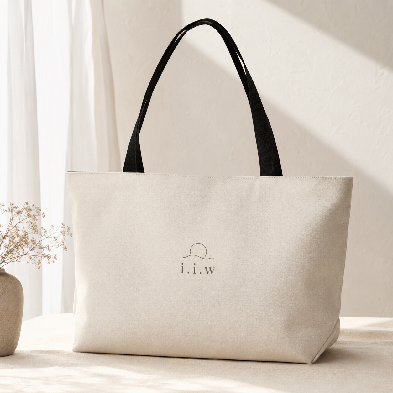 Beige tote bag with black handle on a light surface, featuring a logo.
