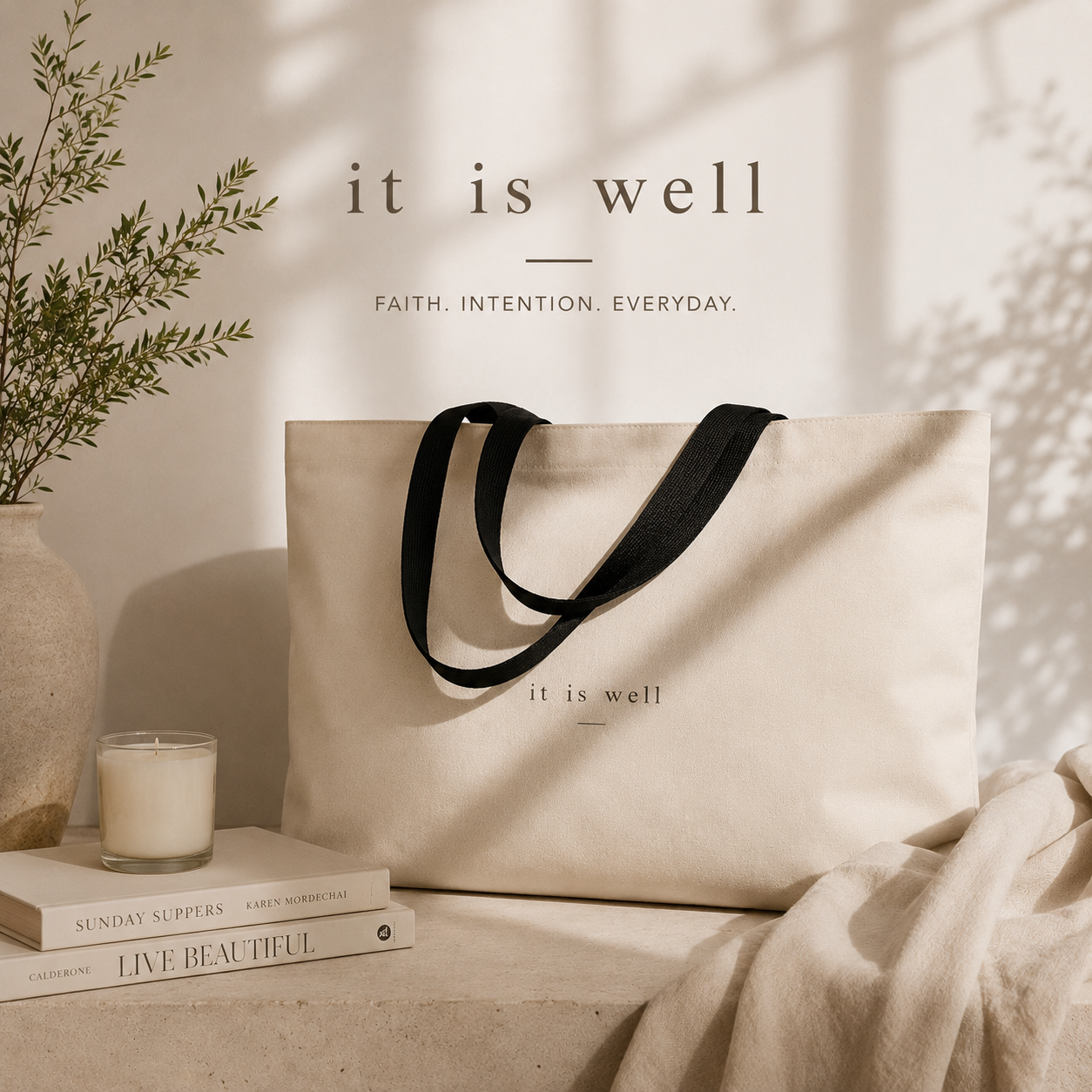 Beige tote bag with 'it is well' text, books, and candle on a neutral background
