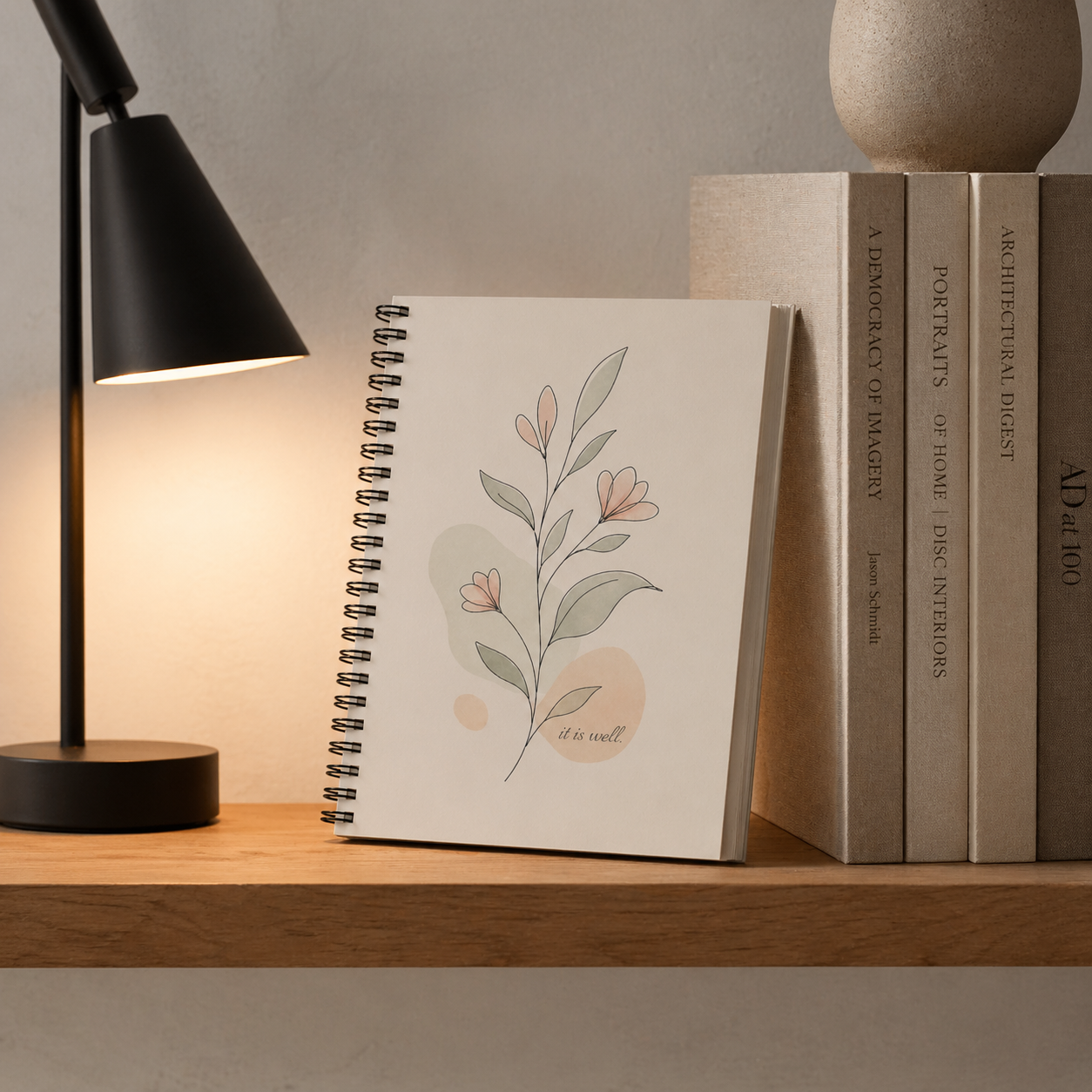 Notebook with floral design on a wooden shelf with books and a lamp.