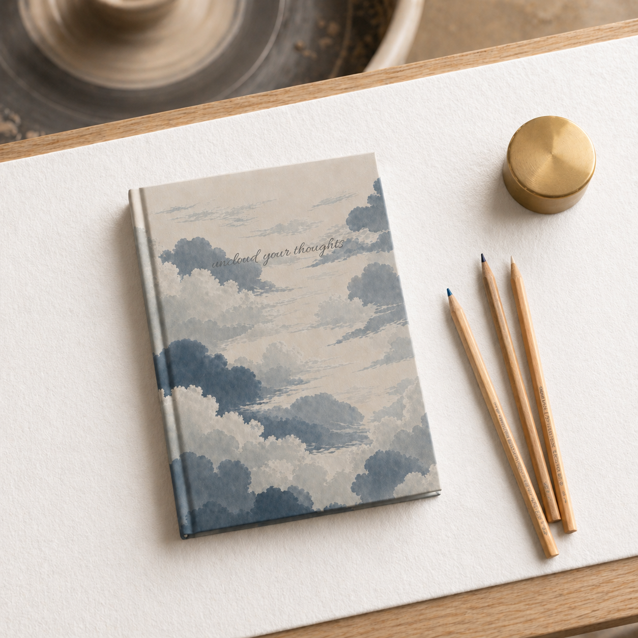 Notebook with cloud design on a white surface with pencils and a gold container.